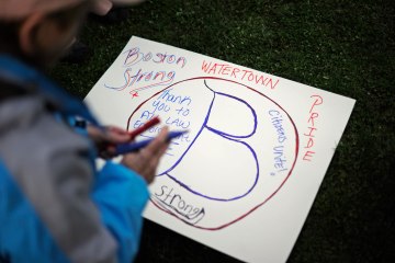 A woman makes a sign during a candlelight vigil for victims of the Boston Marathon bombing at Victory Park in Watertown, Mass.