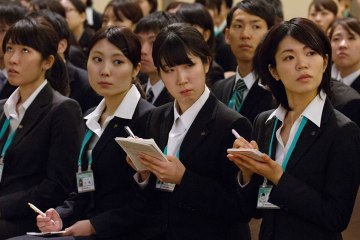 New employees take notes during a speech by Toshifumi Suzuki, chairman and chief executive officer of Seven & I, unseen, at an initiation ceremony in Tokyo, Japan, on Thursday, March 14, 2013.