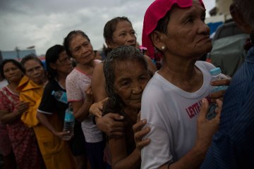 Displaced people effected by Typhoon Haiyan queue in the rain for the first aid delivery at a displacement camp in Tacloban, Philippines on November 14, 2013.